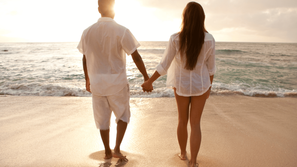 Man and woman holding hands looking at ocean during sunset